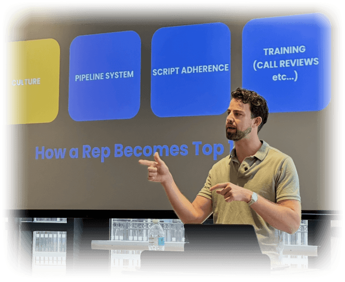 George teaching at a live event, pointing to a slide that reads How a Rep Becomes Top 1%